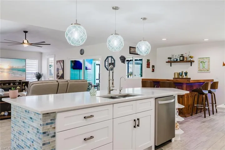 Kitchen featuring light wood-type flooring, white cabinets, open floor plan, dishwasher, and hanging light fixtures