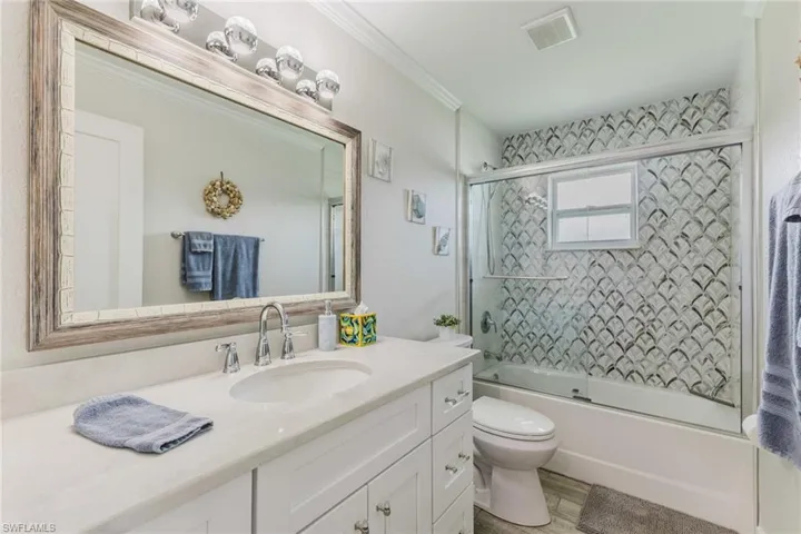 Full bath with vanity, enclosed tub / shower combo, and ornamental molding