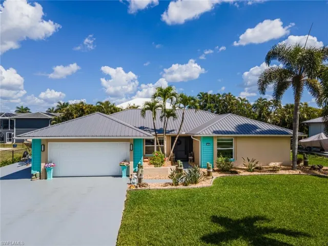 Ranch-style home featuring a metal roof, a garage, driveway, and a front lawn