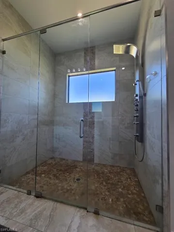 Glass-enclosed shower featuring large format tile walls, a decorative vertical tile accent, and a pebble-style floor