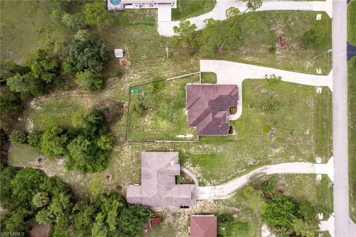 Aerial view showcasing a residential property with a brown-shingled roof and a curved concrete driveway