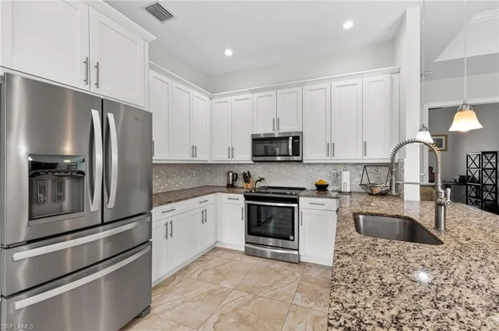 Kitchen featuring white cabinetry, stainless steel appliances, speckled stone countertops, and a tile backsplash