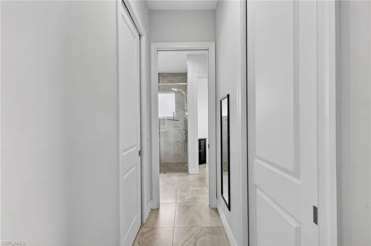 Neutral-toned tile flooring extends through this hallway, featuring crisp white walls and paneled doors