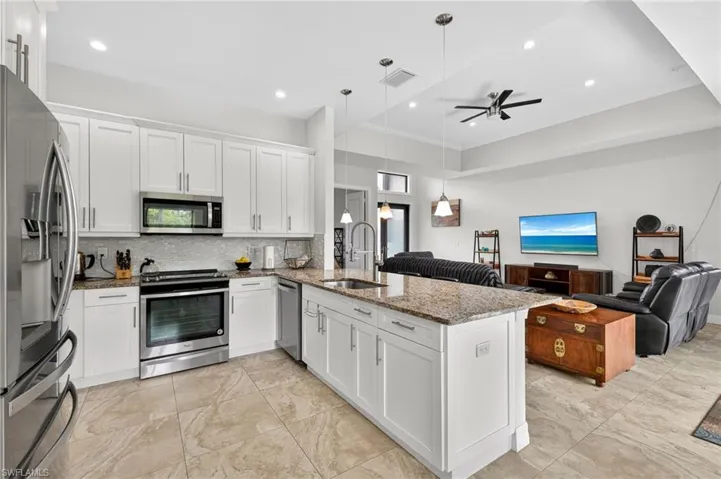 Kitchen featuring white shaker cabinetry, stainless steel appliances, a mosaic tile backsplash, and a large central island with a granite countertop