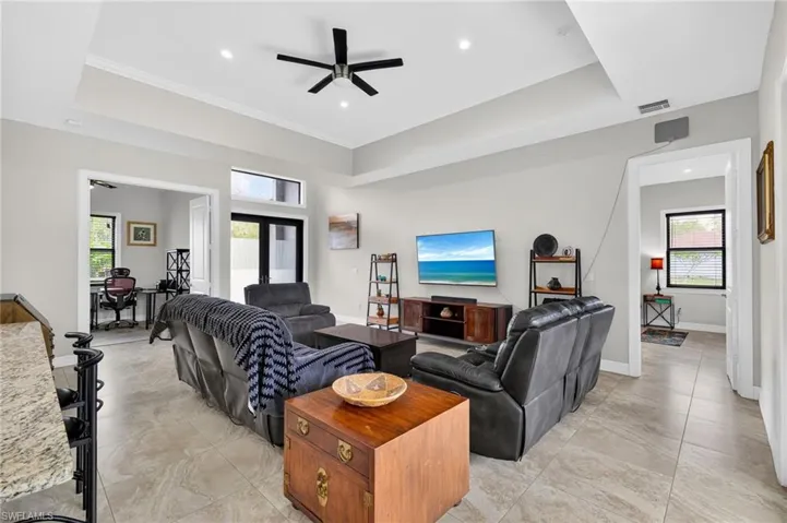 Spacious living area featuring neutral-toned tile flooring, tray ceilings with recessed lighting, and a ceiling fan