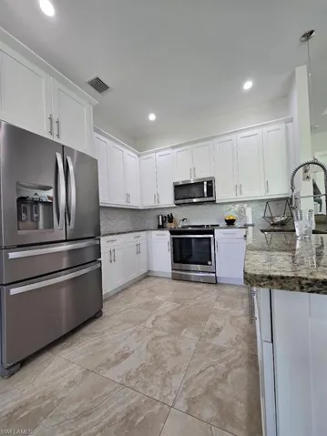 Modern kitchen featuring white shaker cabinetry with brushed nickel hardware, stainless steel appliances, patterned tile flooring, a speckled stone countertop, and recessed lighting