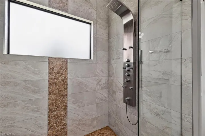 Shower with a multi-function brushed metal shower panel, glass enclosure, and stone-look rectangular wall tiles