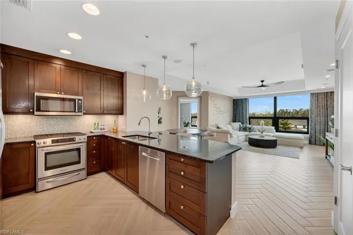 Kitchen with sink, light parquet floors, dark stone countertops, hanging light fixtures, and stainless steel appliances