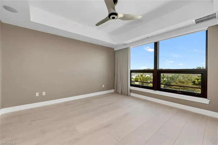 Master Bedroom featuring ceiling fan, light wood flooring, updated window treatment , impact resistant windows, freshly painted walls and a tray ceiling