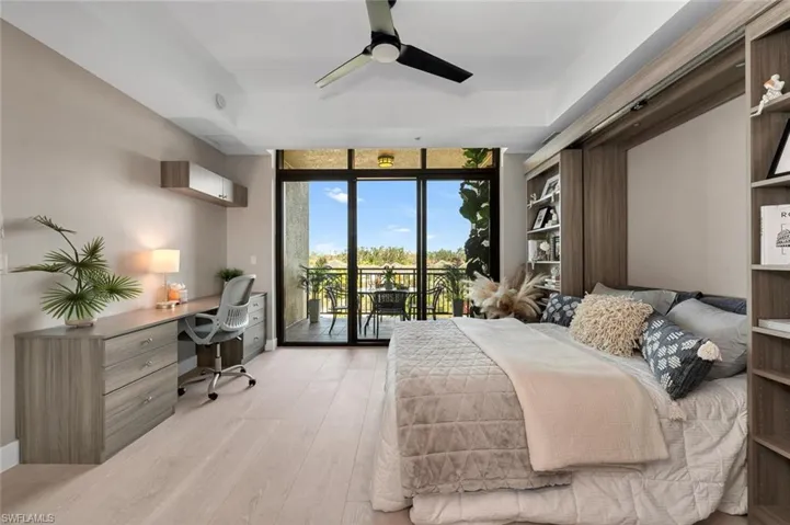 Bedroom featuring built in desk, a wall of windows, access to exterior, ceiling fan, and light wood-type flooring