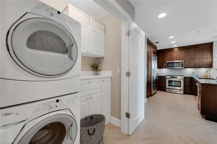 Clothes washing area featuring stacked washer and dryer, sink, and light parquet floors
