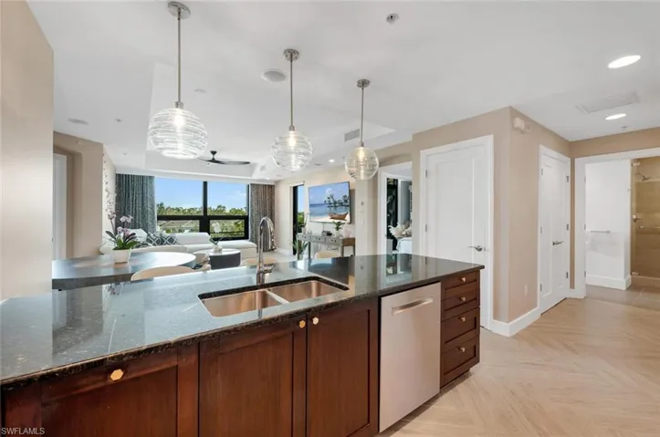 Kitchen featuring decorative light fixtures, sink, stainless steel dishwasher, and dark stone counters
