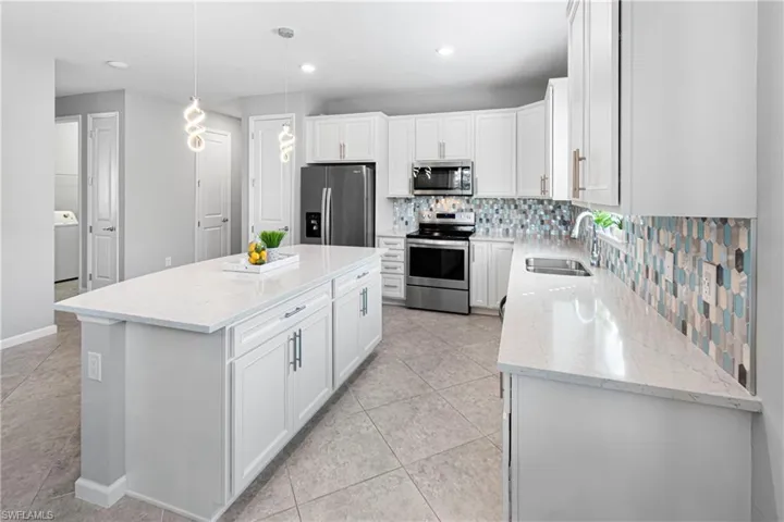 Kitchen featuring sink, a kitchen island, pendant lighting, stainless steel appliances, and white cabinets