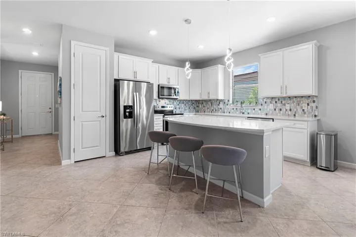 Kitchen with stainless steel appliances, a kitchen island, hanging light fixtures, and white cabinets