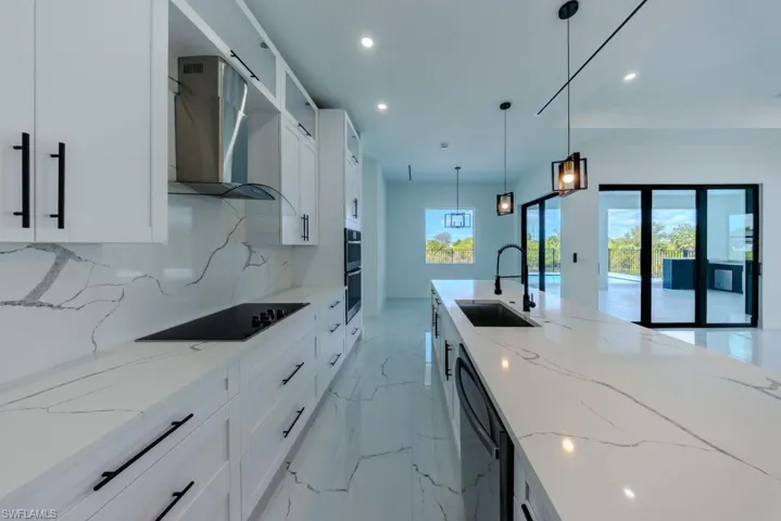 Kitchen with white cabinetry, light stone countertops, hanging light fixtures, black appliances, and light marble finish floors