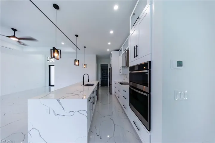 Kitchen featuring a large island with sink, light stone countertops, stainless steel appliances, light marble finish flooring, and white cabinets