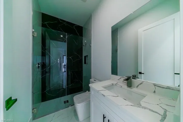 Full bath featuring vanity, a marble finish shower, and light marble finish flooring