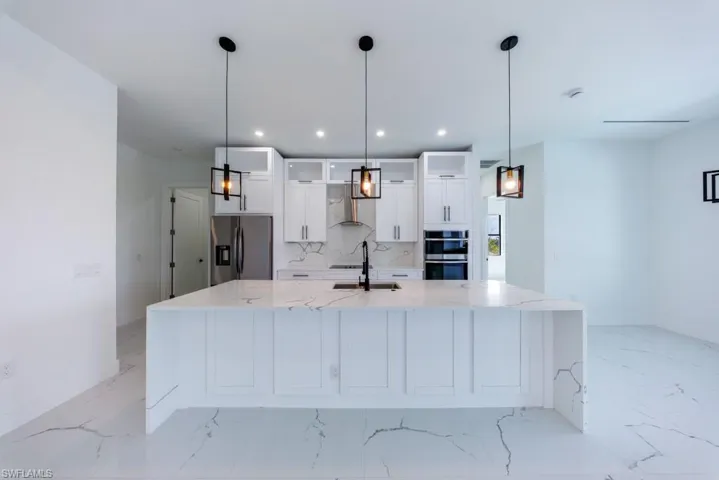 Kitchen with white cabinets, light stone counters, glass insert cabinets, stainless steel appliances, and a large island with sink