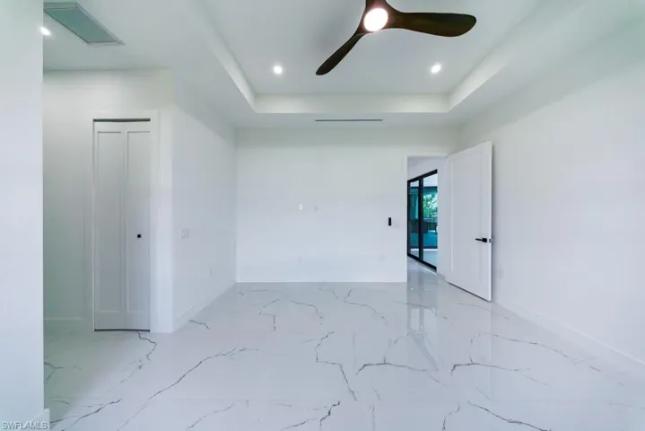 Spare room featuring a tray ceiling, a ceiling fan, and light marble finish floors