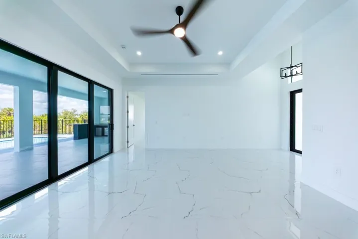 Unfurnished room featuring ceiling fan, light marble finish floors, a tray ceiling, and recessed lighting