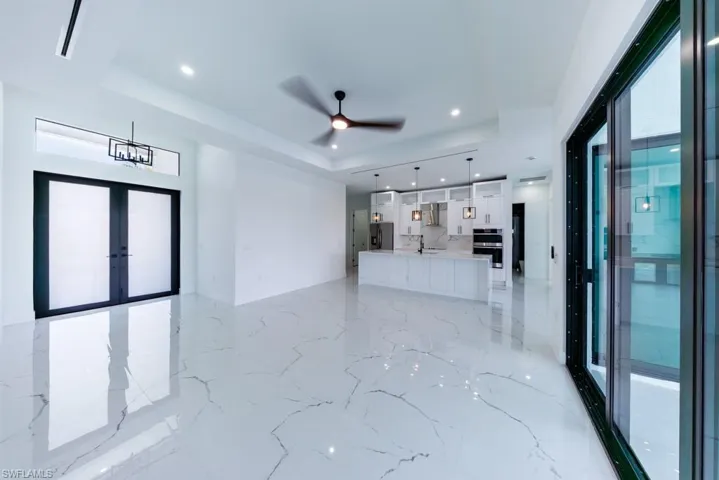 Unfurnished living room featuring french doors, ceiling fan, recessed lighting, light marble finish floors, and a tray ceiling