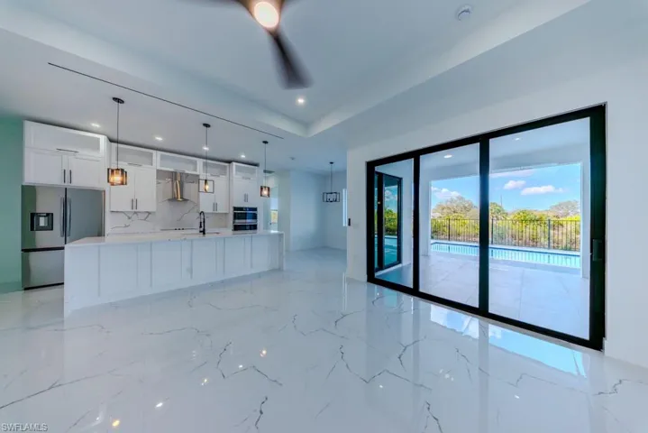 Kitchen featuring white cabinets, stainless steel appliances, decorative light fixtures, a large island with sink, and light stone counters