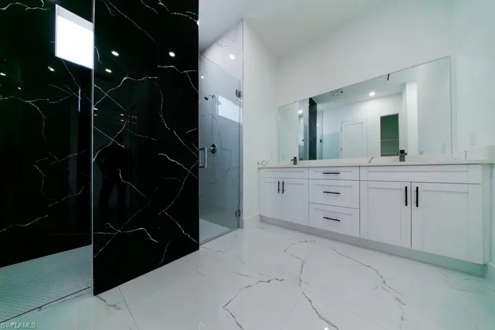 Full bath with a marble finish shower, double vanity, and light marble finish flooring