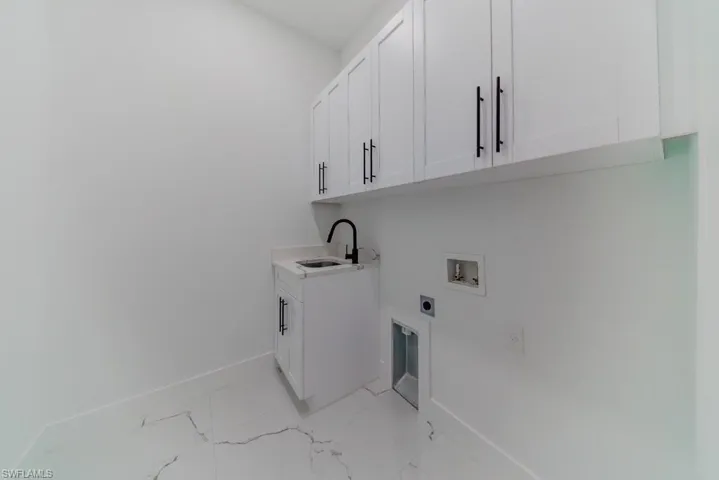 Laundry area with cabinet space, hookup for a washing machine, hookup for an electric dryer, and light marble finish flooring