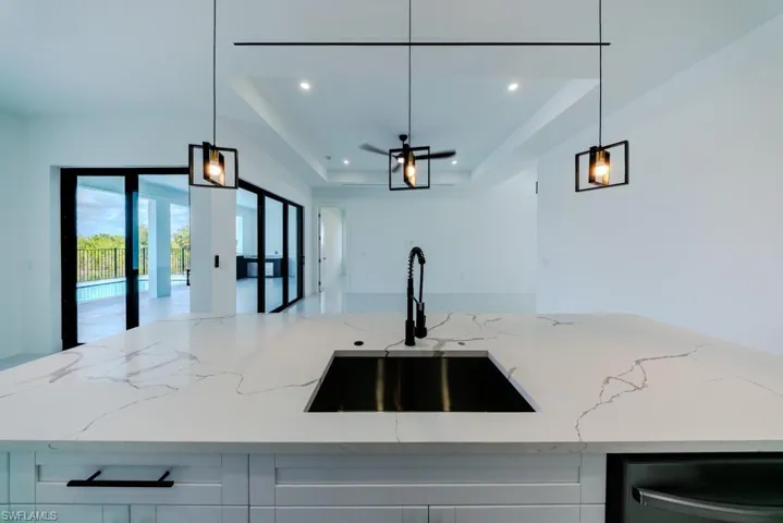 Kitchen with light stone countertops, a center island with sink, white cabinetry, hanging light fixtures, and a tray ceiling