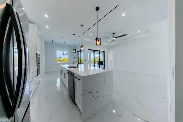 Kitchen featuring white cabinetry, freestanding refrigerator, a large island, open floor plan, and light stone counters
