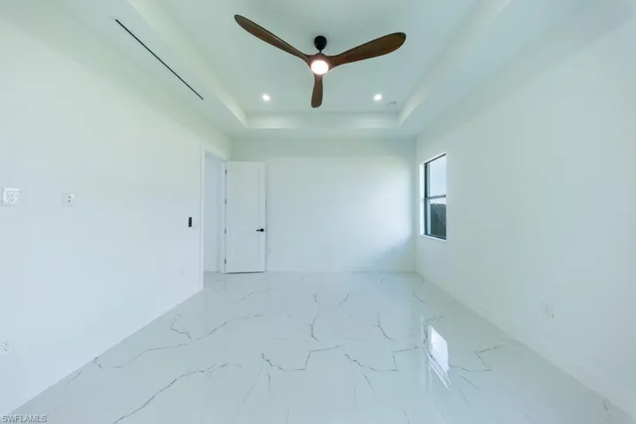 Spare room with light marble finish floors, a ceiling fan, recessed lighting, and a tray ceiling
