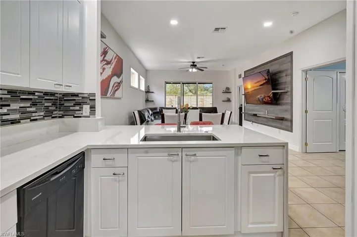 Kitchen with kitchen peninsula, white cabinets, black dishwasher, and sink