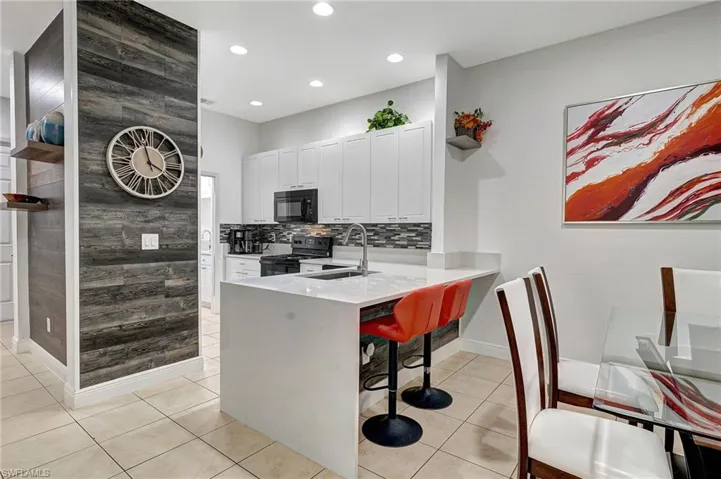 Kitchen with kitchen peninsula, a breakfast bar, light tile patterned floors, black appliances, and white cabinetry