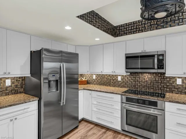 Kitchen with white cabinets, stainless steel appliances, dark stone countertops, and light hardwood / wood-style floors
