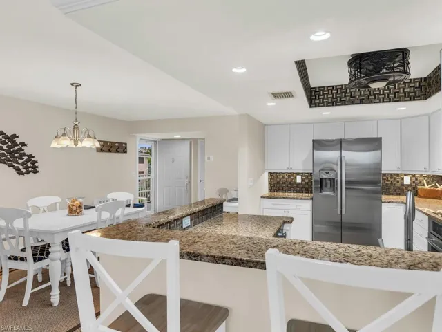 Kitchen featuring decorative light fixtures, white cabinetry, dark stone countertops, stainless steel fridge, and a breakfast bar area