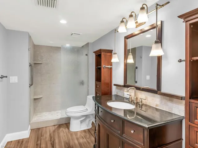 Bathroom featuring a tile shower, hardwood / wood-style flooring, toilet, vanity, and decorative backsplash