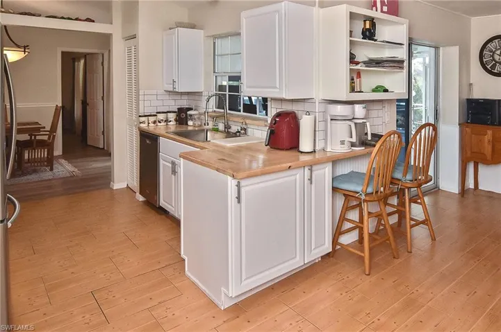 Kitchen with wooden counters, white cabinetry, tasteful backsplash, light wood-type flooring, and stainless steel dishwasher
