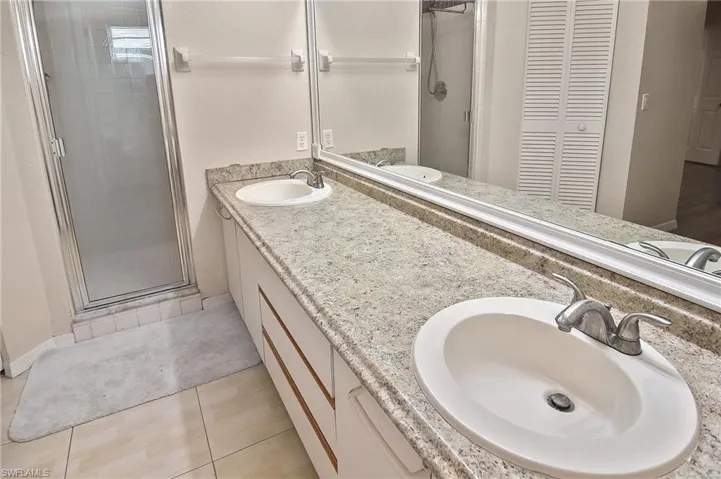 Bathroom featuring tile patterned flooring, dual vanity, and an enclosed shower