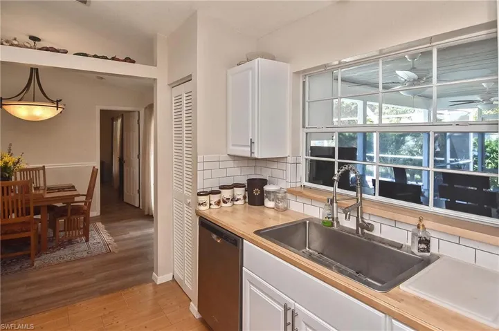 Kitchen with light hardwood / wood-style flooring, tasteful backsplash, white cabinets, decorative light fixtures, and stainless steel dishwasher