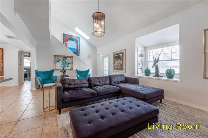 Living room with a notable chandelier, baseboards, light tile patterned floors, visible vents, and high vaulted ceiling
