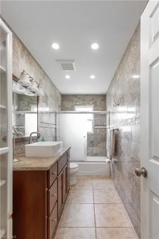 Bathroom featuring tile walls, tile patterned flooring, vanity, toilet, and enclosed tub / shower combo