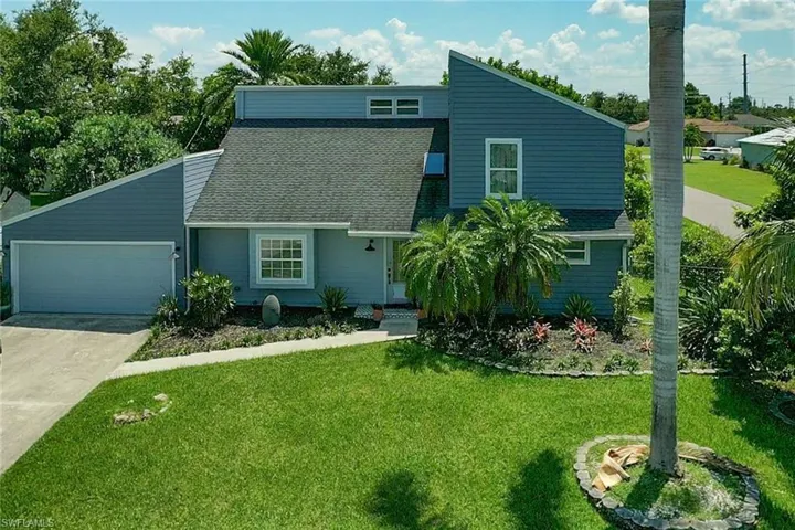 Mid-century modern home featuring concrete driveway, roof with shingles, an attached garage, and a front yard