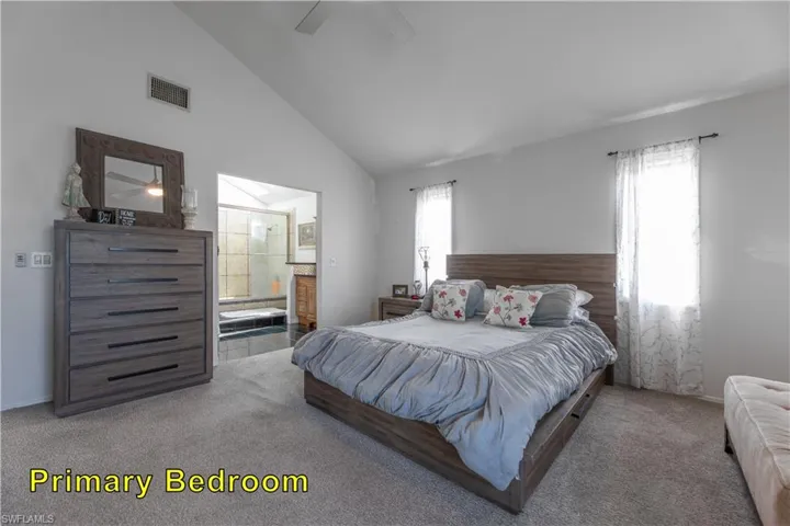 Carpeted bedroom featuring visible vents, a ceiling fan, connected bathroom, and high vaulted ceiling