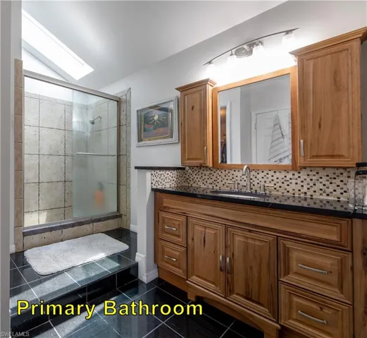Bathroom with vanity, decorative backsplash, a skylight, and a shower stall