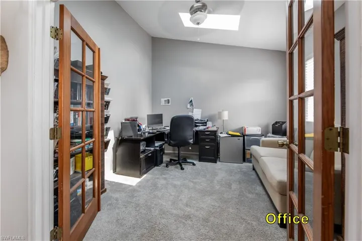 Home office featuring carpet flooring, a ceiling fan, a skylight, and french doors