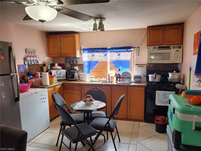 Kitchen with wood finish cabinetry, black gas range, white microwave, freestanding refrigerator, and a textured ceiling