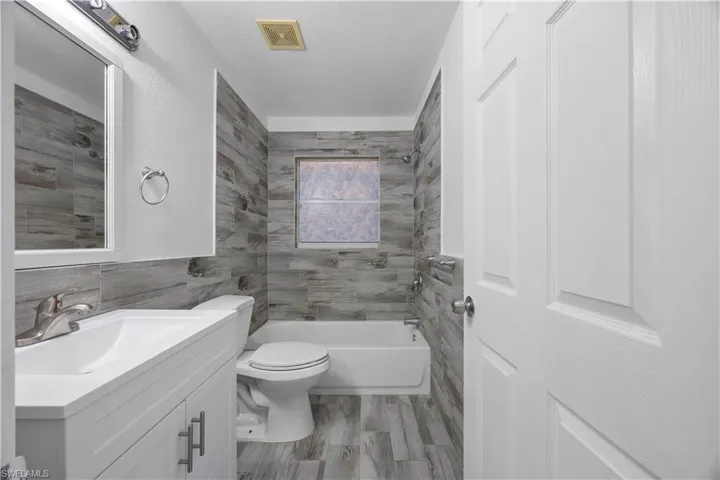 Full bathroom with tile walls, vanity, toilet, shower / tub combination, and a textured ceiling