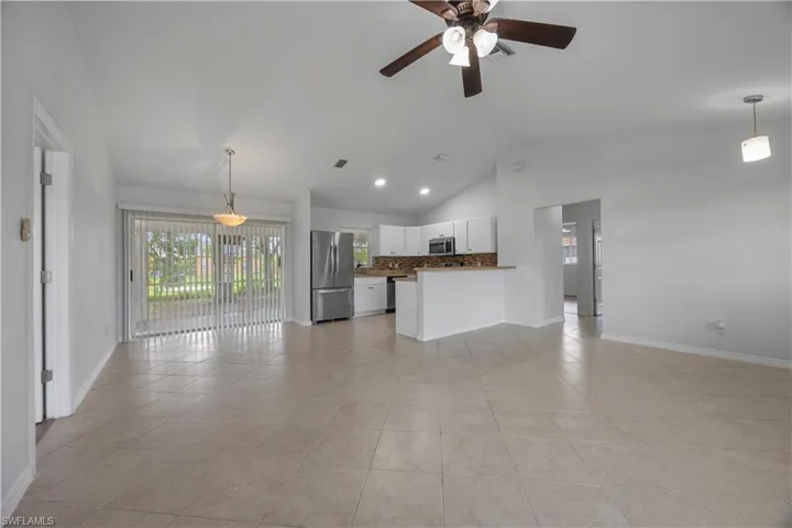 Unfurnished living room with lofted ceiling, a ceiling fan, light tile patterned flooring, and baseboards