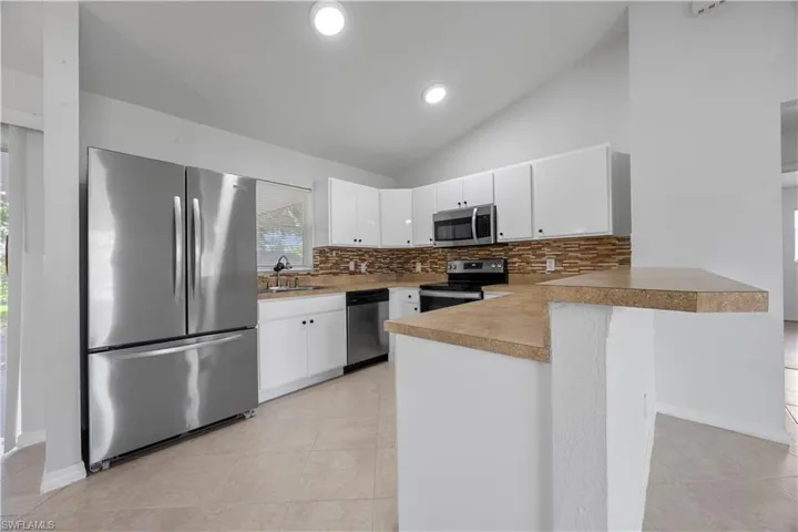Kitchen featuring appliances with stainless steel finishes, a peninsula, tasteful backsplash, a sink, and light tile patterned floors