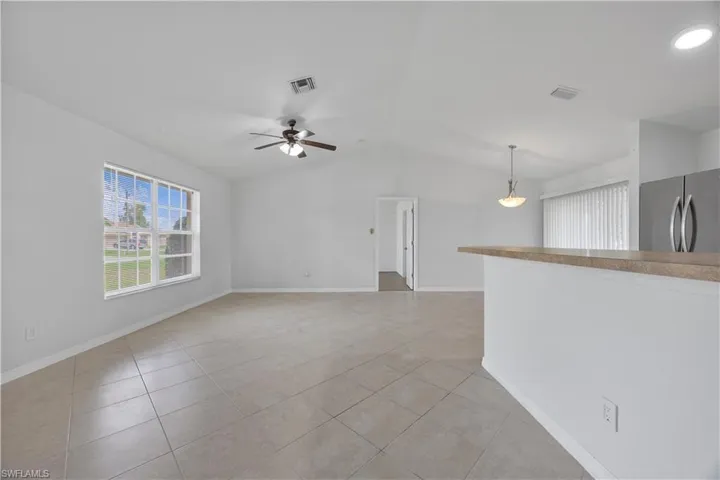 Unfurnished living room with light tile patterned flooring, lofted ceiling, a ceiling fan, and baseboards